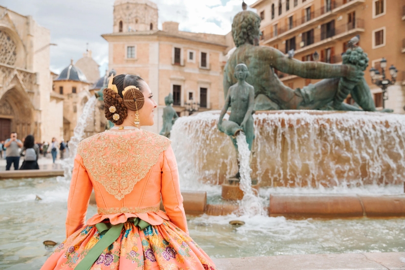 Mujer vestida de fallera mirando a fuente de Valencia